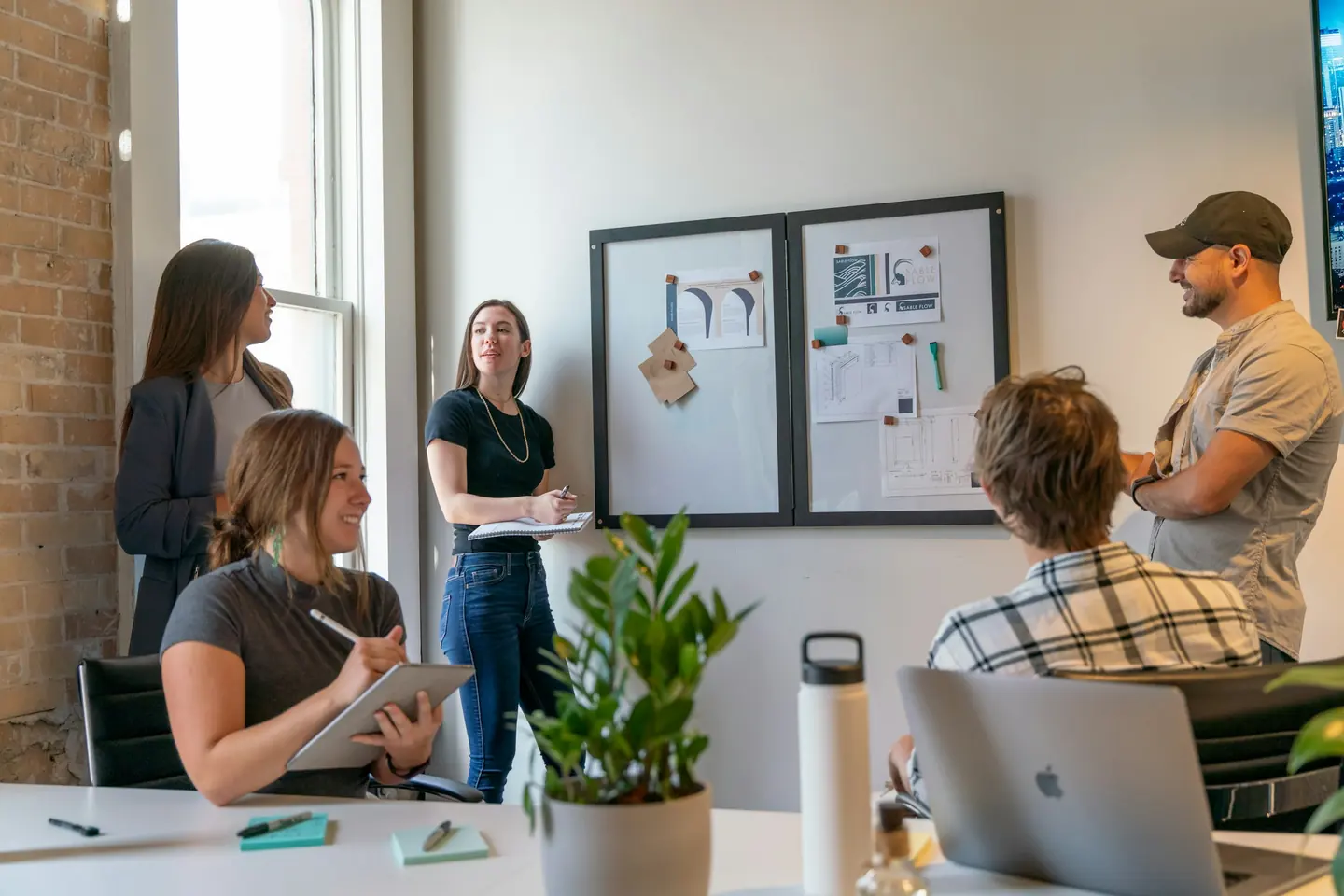 An agency team reviews work together around a table in a sunlit studio.